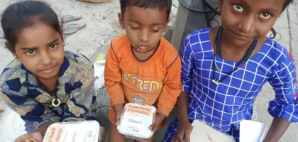 Two girls and one boy sitting on the road, holding food packets distributed by an AAPKE SAATH Foundation volunteer during the 'Food for Every Breath' campaign.