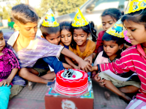 A group of underprivileged children wearing birthday hats, joyfully cutting a birthday cake together during a celebration organized by Aapke Saath Foundation.