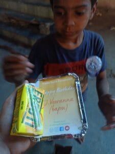 A boy happily receiving food and fruit during a distribution event in Delhi.