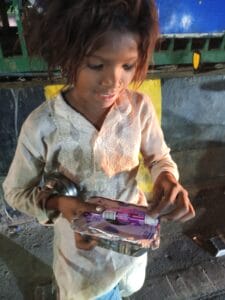 A girl smiling with joy as she receives a food packet and chocolate during a distribution event in Delhi.