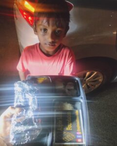 Young boy receiving food from a volunteer on the street at night, expressing hope and happiness.