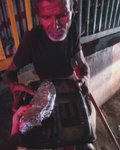 An elderly man with a walking stick receives food from an AAPKE SAATH Foundation volunteer during a night-time food distribution campaign.