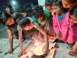 9-10 children lighting a candle on a birthday cake with 'Happy Birthday Nawaz' written on it. The cake is donated by a donor to celebrate their special day with the children, who are smiling and happy.