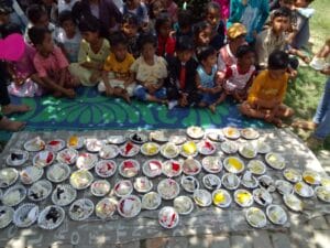 Children sitting on a mat in front of plates with cake, organized by AAPKE SAATH Foundation, waiting for the cake distribution.