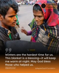 A volunteer kneels down to give a warm blanket to an elderly woman, while others in the community receive winter essentials like caps and socks during the distribution drive.